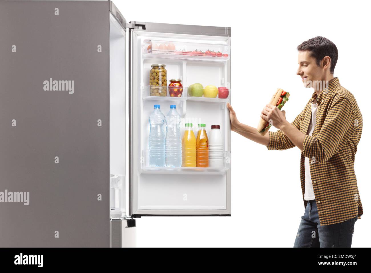 Homme affamé avec un sandwich devant un réfrigérateur isolé sur fond blanc Banque D'Images