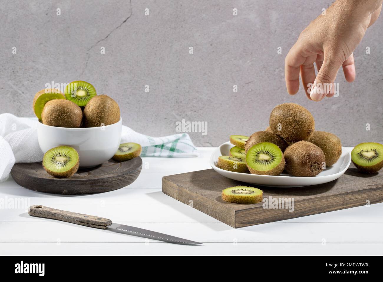 Prenez à la main un kiwi frais d'une assiette blanche sur une base en bois blanc. Banque D'Images