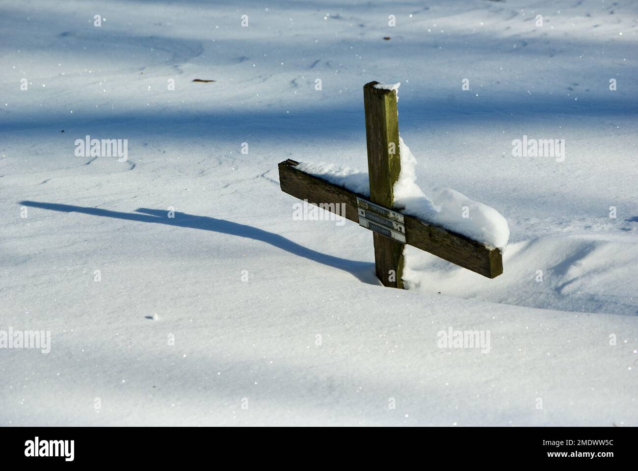 La croix en bois de l'ancien chrétien avec son ombre dans une forte dérive de neige sur le cimetière en hiver. Banque D'Images