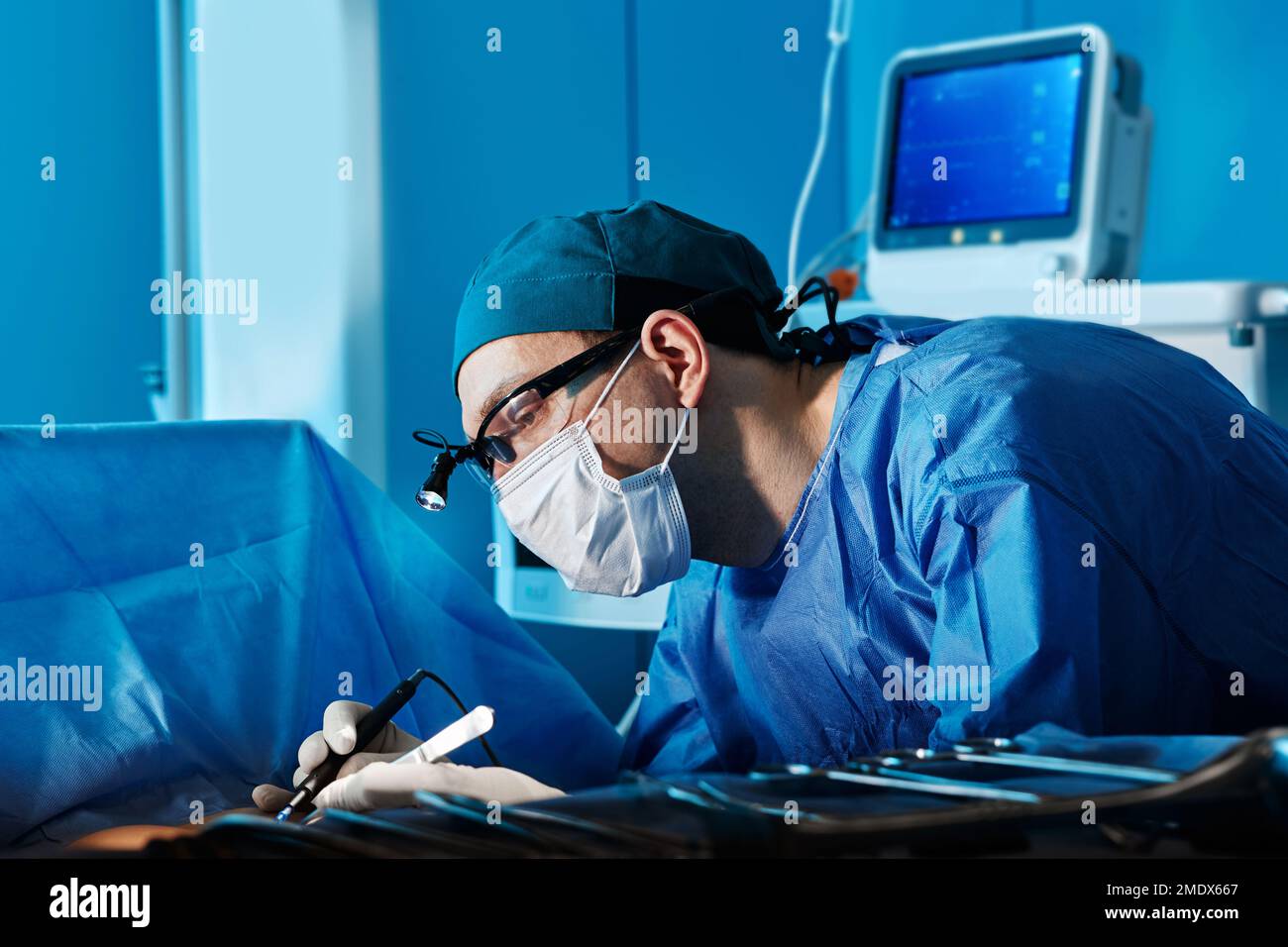 Portrait d'un chirurgien ciblé portant un masque facial et un phare de protection pendant son fonctionnement dans le bloc opératoire de l'hôpital. Profession de chirurgien Banque D'Images