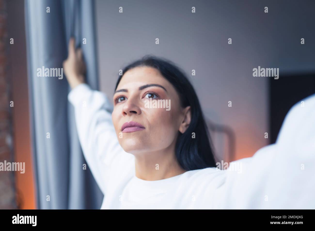 Gros plan d'une femme caucasienne tenant des rideaux de fenêtre et regardant à l'extérieur. Photo de haute qualité Banque D'Images