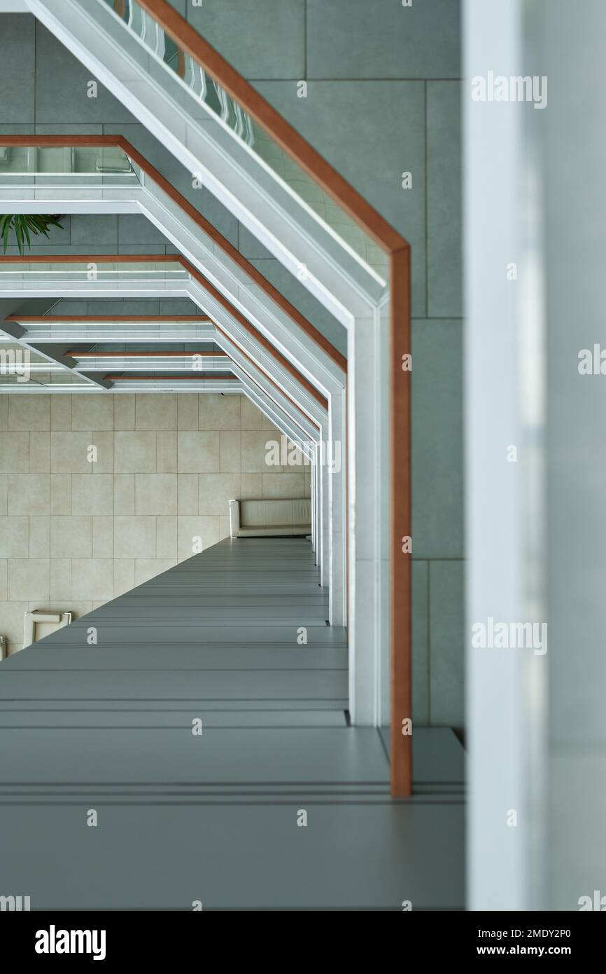 Vue de dessus de l'intérieur d'un bâtiment de plusieurs étages avec garde-corps de clôture, sol carrelé gris, panneaux muraux et une partie des fenêtres des bureaux à espace ouvert Banque D'Images