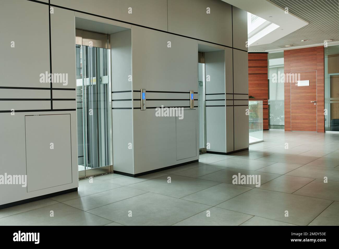 Couloir vide du centre d'affaires high-tech avec deux ascenseurs, sol carrelé gris et porte marron du directeur du bureau de l'entreprise Banque D'Images