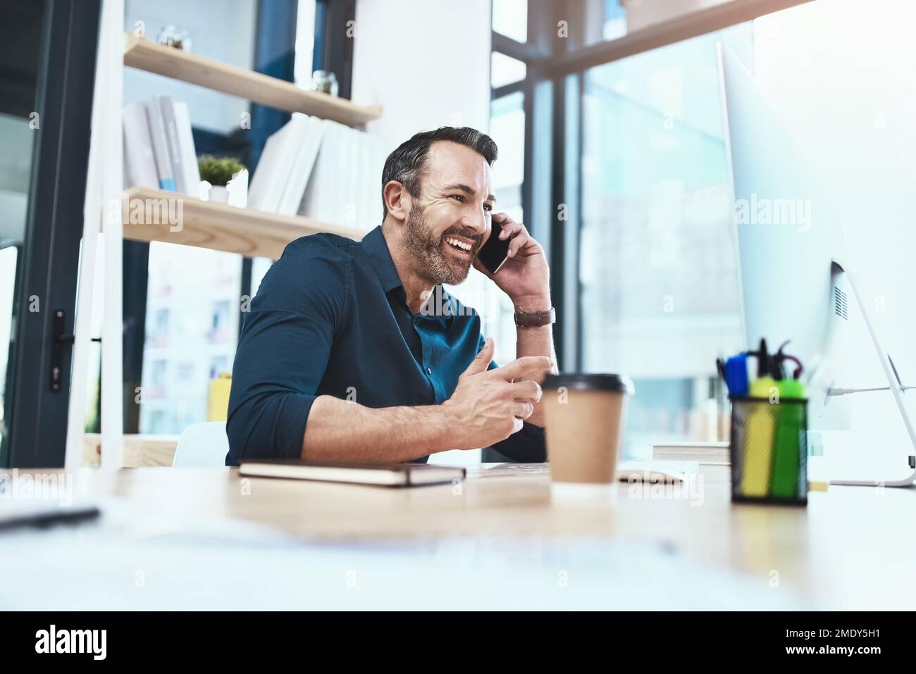 Appelez-le pour tous vos besoins créatifs. un homme d'affaires mature parlant au téléphone tout en étant assis à son bureau. Banque D'Images
