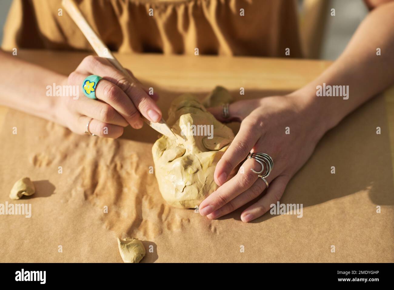 Mains de jeune femme créative avec outil en bois couper les yeux sur le visage de la figurine humaine en argile tout en étant assis sur le lieu de travail dans le studio à la maison Banque D'Images