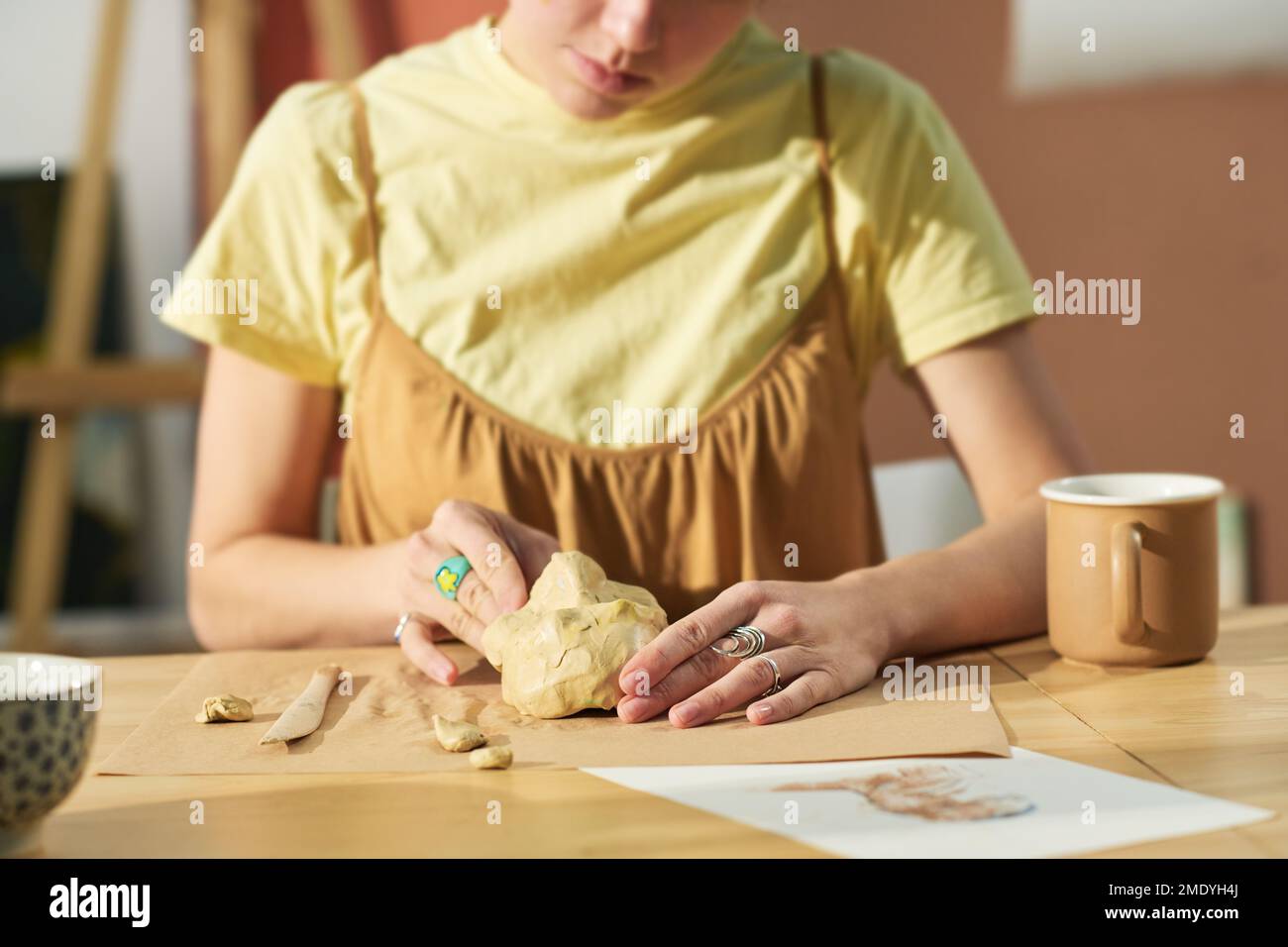 Gros plan de jeunes artisans créatifs faisant face humaine de morceau d'argile tout en étant assis sur le lieu de travail avec toutes les fournitures nécessaires Banque D'Images