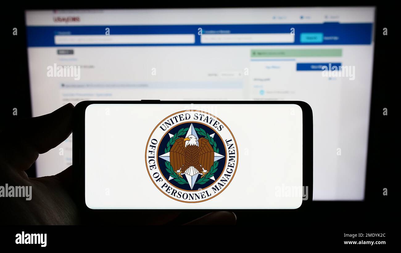 Personne tenant un téléphone portable avec le sceau de l'Office of personnel Management (OPM) des États-Unis sur l'écran en face de la page Web. Mise au point sur l'affichage du téléphone. Banque D'Images