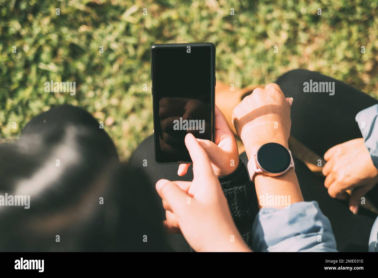Heureux amis partageant du contenu multimédia en ligne avec leurs smartphones et SmartWatch, deux belles femmes Latina assis à l'extérieur Banque D'Images