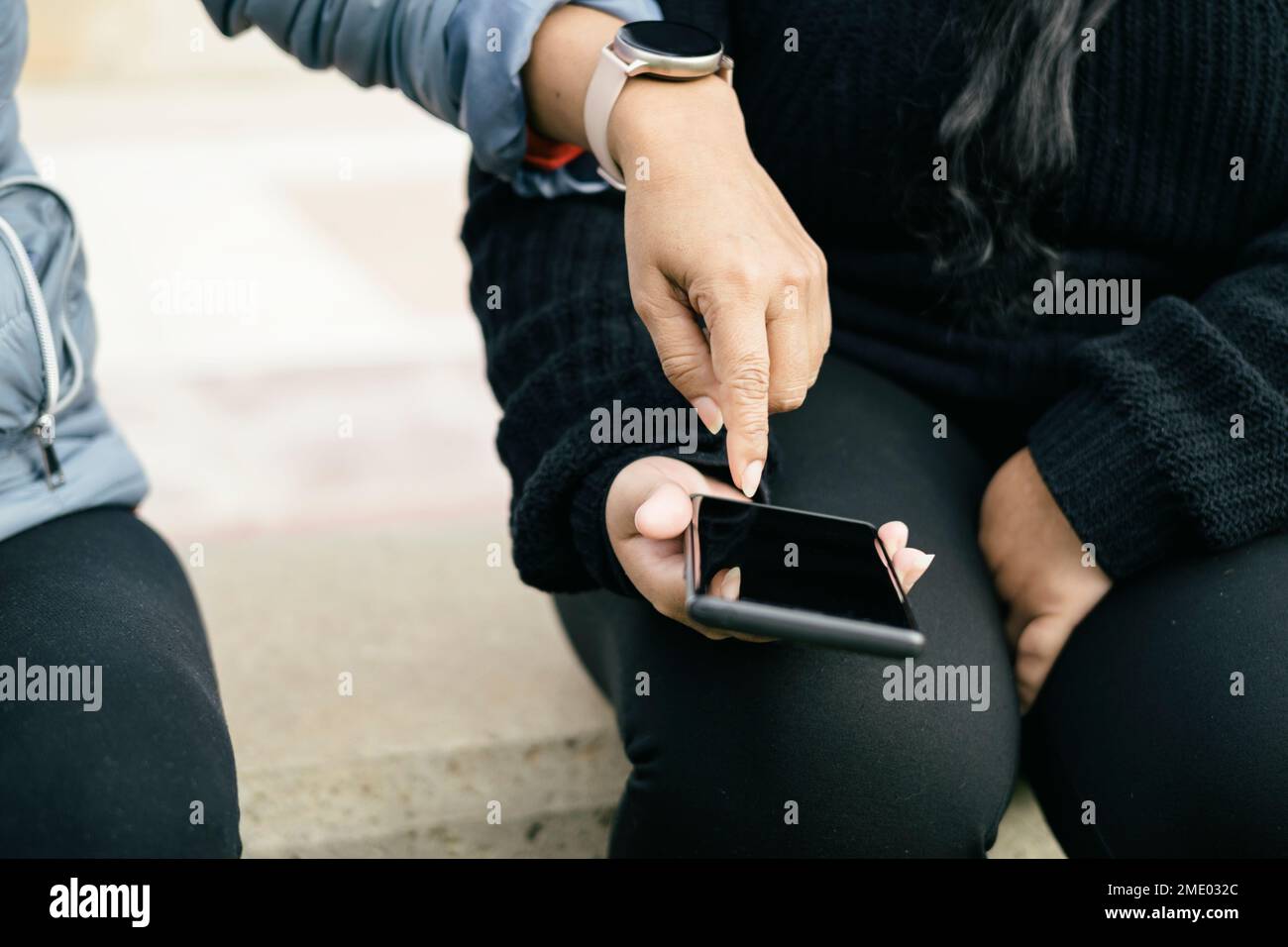 main d'une femme avec une montre intelligente pointant vers un smartphone, tenant dans la main jeune femme latina, vue avant sans visages reconnaissables Banque D'Images
