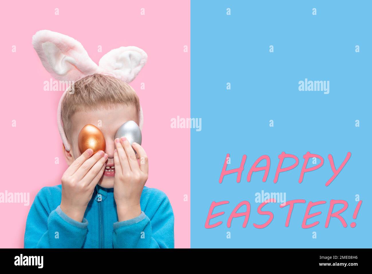 Un petit garçon gai dans une veste bleue et avec des oreilles de lapin tient des oeufs de Pâques colorés sur un fond bleu-rose avec le texte Joyeuses Pâques. Le bu de Pâques Banque D'Images