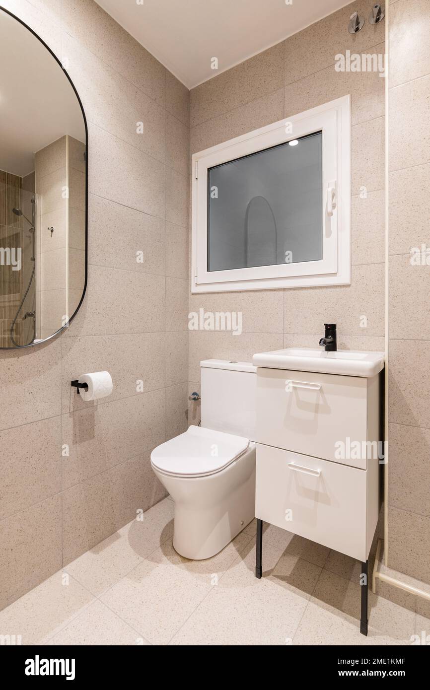 Partie de la salle de bains avec cuvette de toilette, lavabo sur table,  beau miroir ovale sur le mur bordé de carreaux de marbre beige, dans lequel  vous pouvez voir le reflet