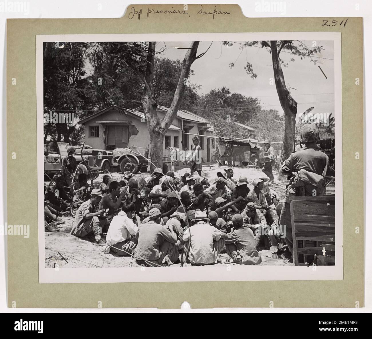 Des prisonniers de guerre japonais sont vus blottis sur le sol à Saipan, mangeant des rations tout en étant gardés par la police militaire américaine. Ces prisonniers ont été capturés lors de la poussée nord de l’armée américaine sur le théâtre du Pacifique. Banque D'Images