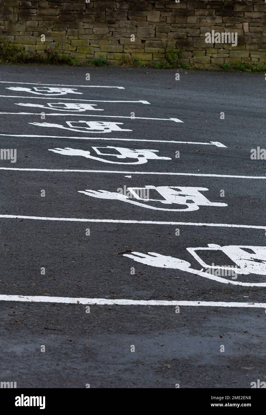 Une rangée de baies pour véhicules électriques. Les baies montrent le symbole officiel du ministère des Transports pour une voiture électrique peinte sur le tarmac. Banque D'Images
