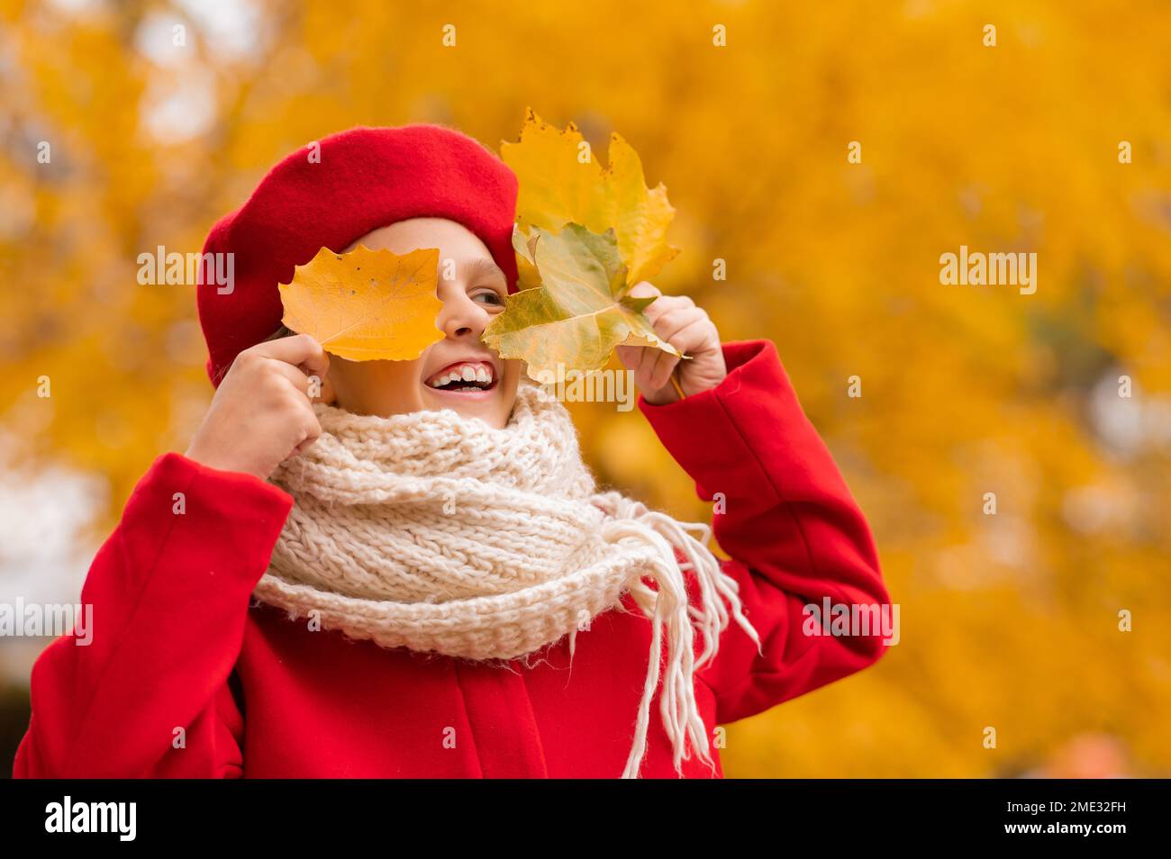 Une heureuse fille de race blanche, sous un manteau rouge, et une béret qui marche dans le parc en automne ferme les yeux avec des feuilles d'érable. Banque D'Images Une heureuse fille de race blanche, sous un manteau rouge, et une béret qui marche dans le parc en automne ferme les yeux avec des feuilles d'érable. Banque D'Images