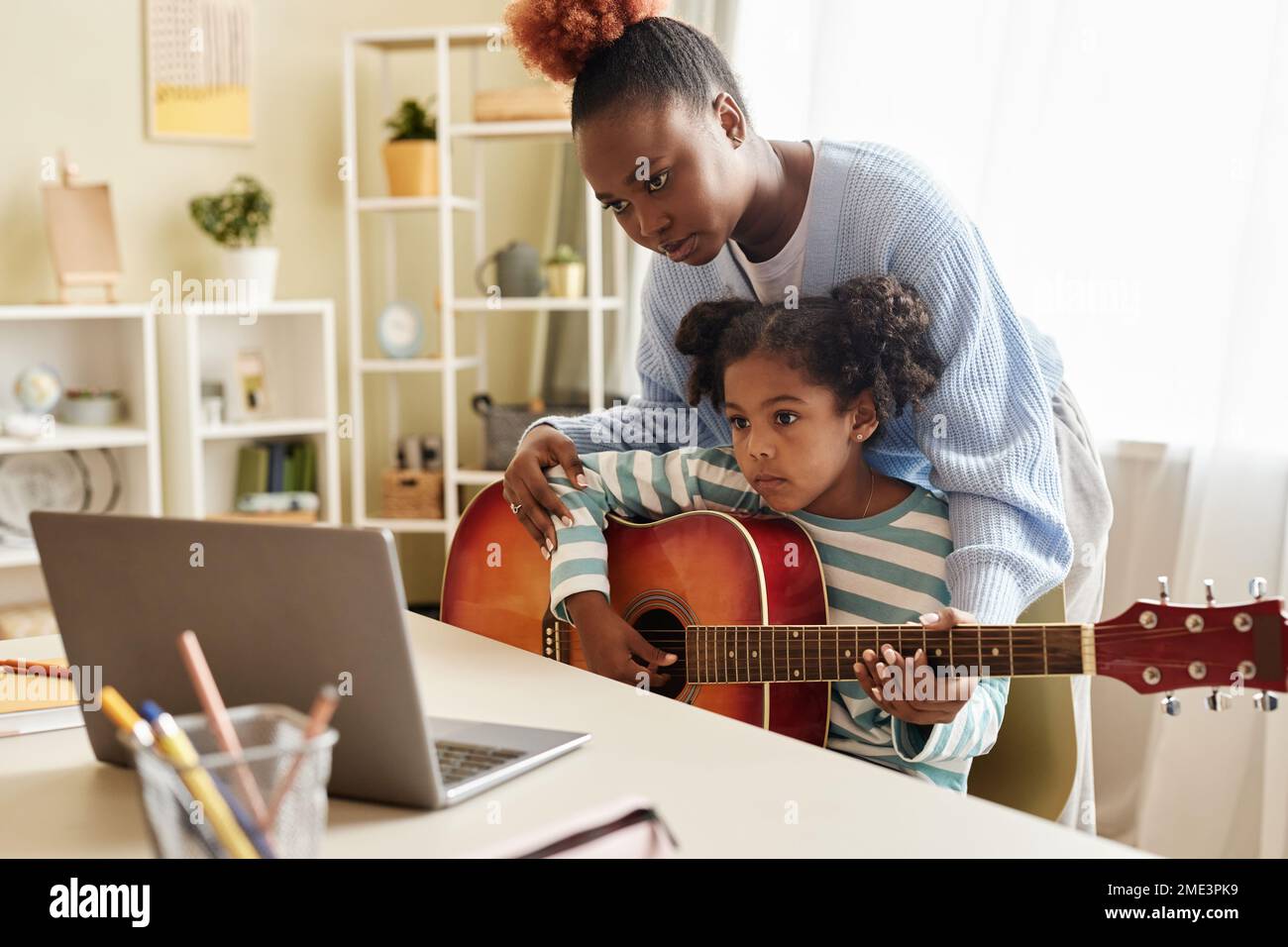 Portrait de petite fille noire regardant la leçon de musique en ligne avec la mère et jouant de la guitare à la maison Banque D'Images