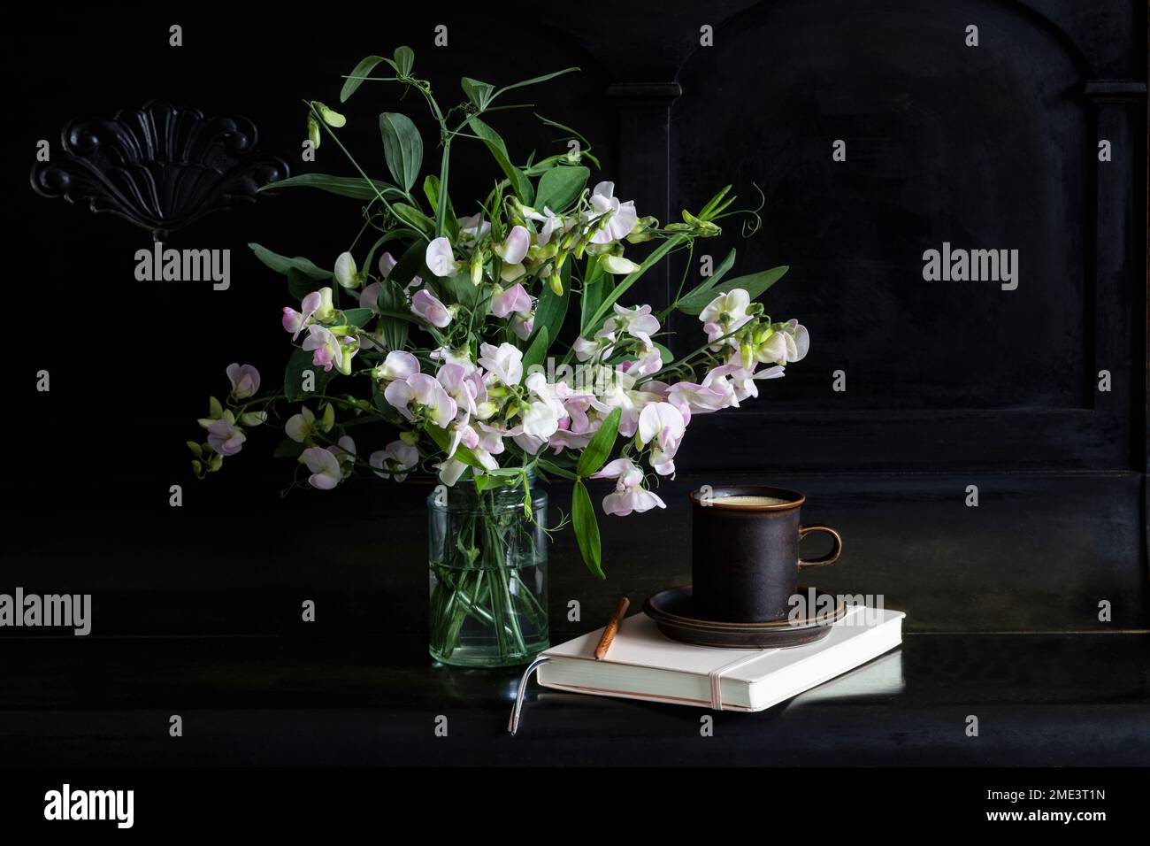 Fleurs de pois suétés dans un pot en verre par tasse de café et journal sur piano noir Banque D'Images