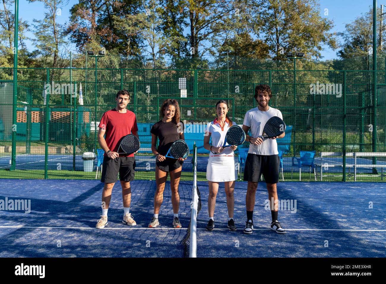 Des hommes et des femmes heureux avec des raquettes de paddle-tennis debout sur le terrain de sport Banque D'Images