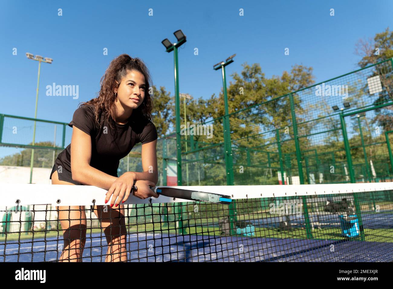 Jeune femme avec raquette penchée sur le filet de tennis Banque D'Images