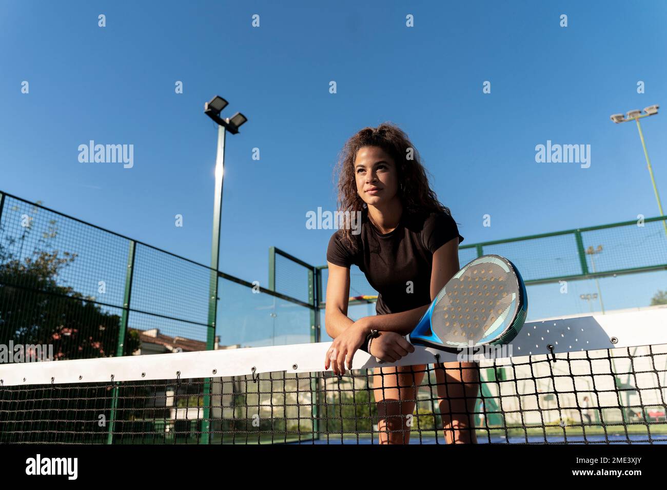 Jeune femme avec raquette penchée sur le filet de tennis au court Banque D'Images