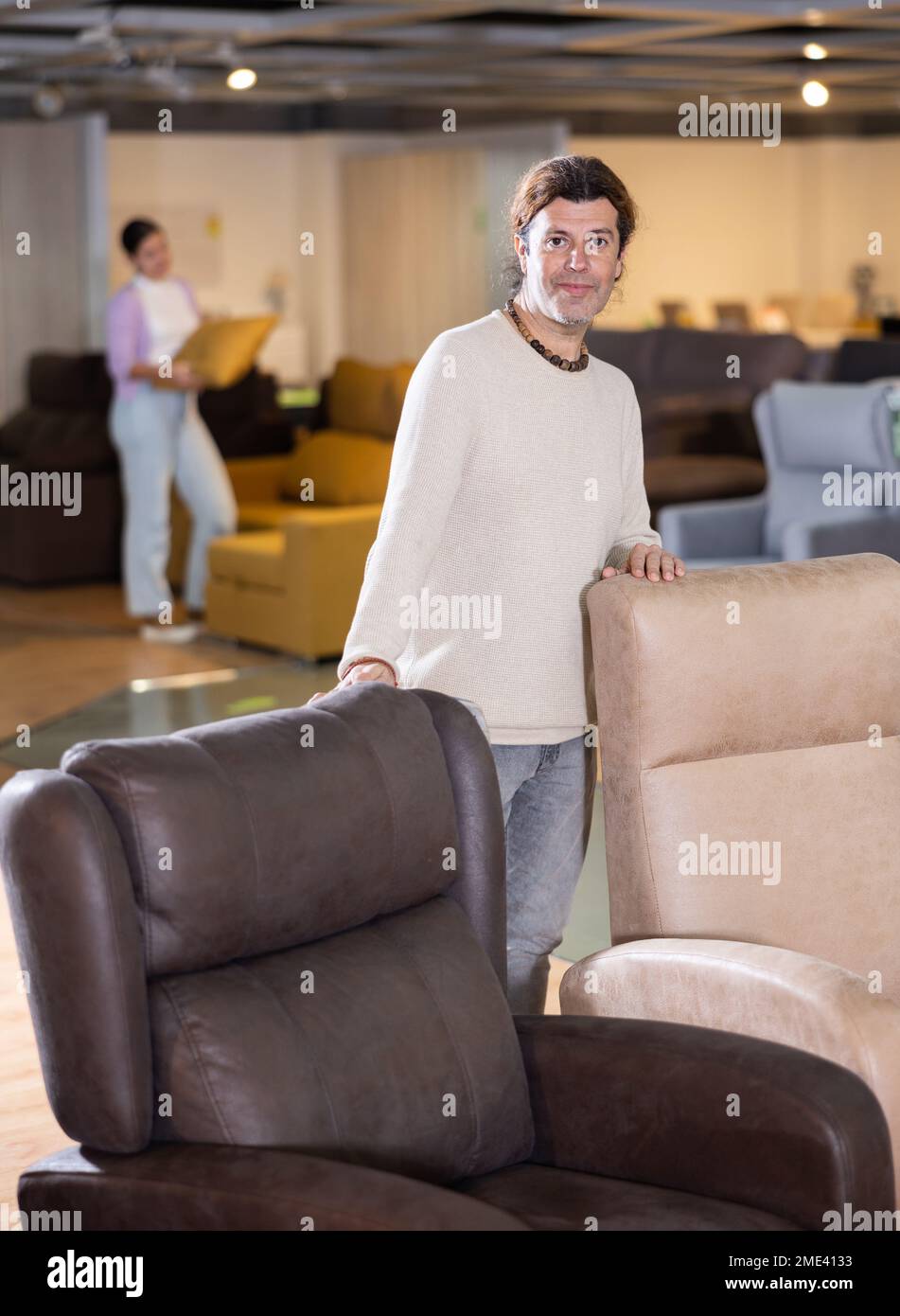 Un vendeur de meubles de sexe masculin présente des fauteuils à vendre dans une salle d'exposition de meubles Banque D'Images