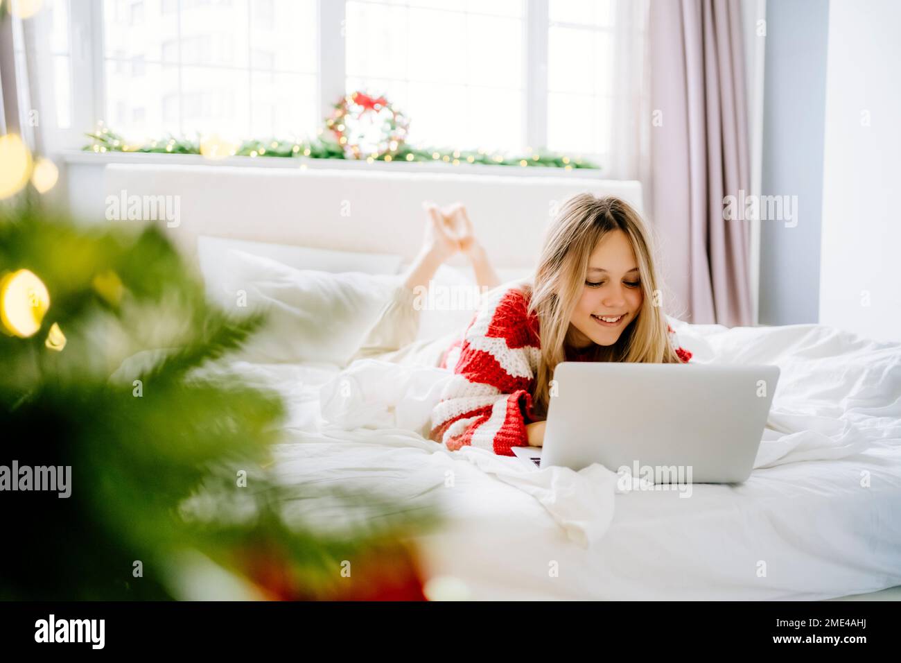 Bonne fille couchée sur le lit à l'aide d'un ordinateur portable à la maison Banque D'Images