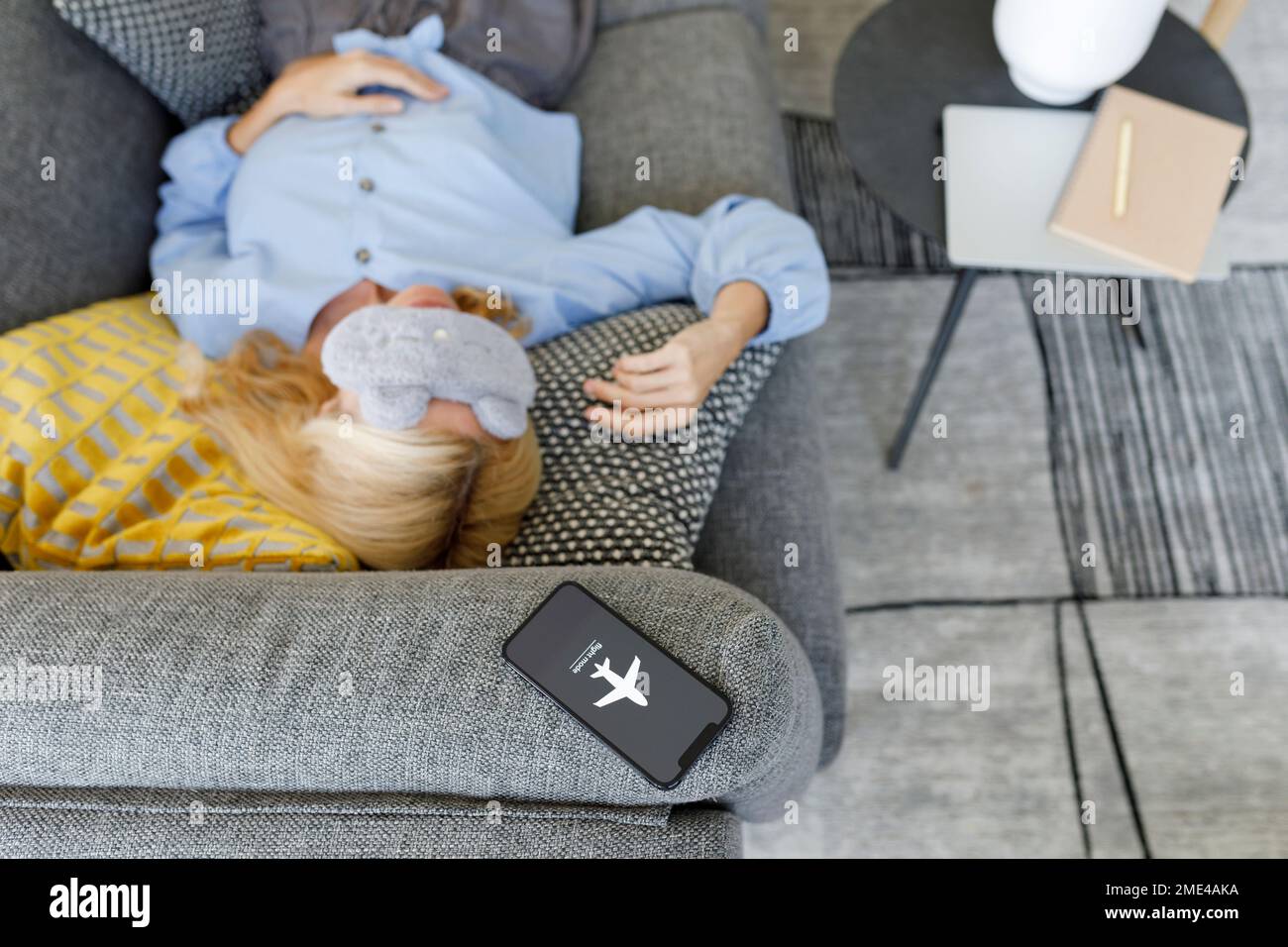 Femme portant un masque oculaire dormant sur un canapé avec un smartphone en mode avion Banque D'Images