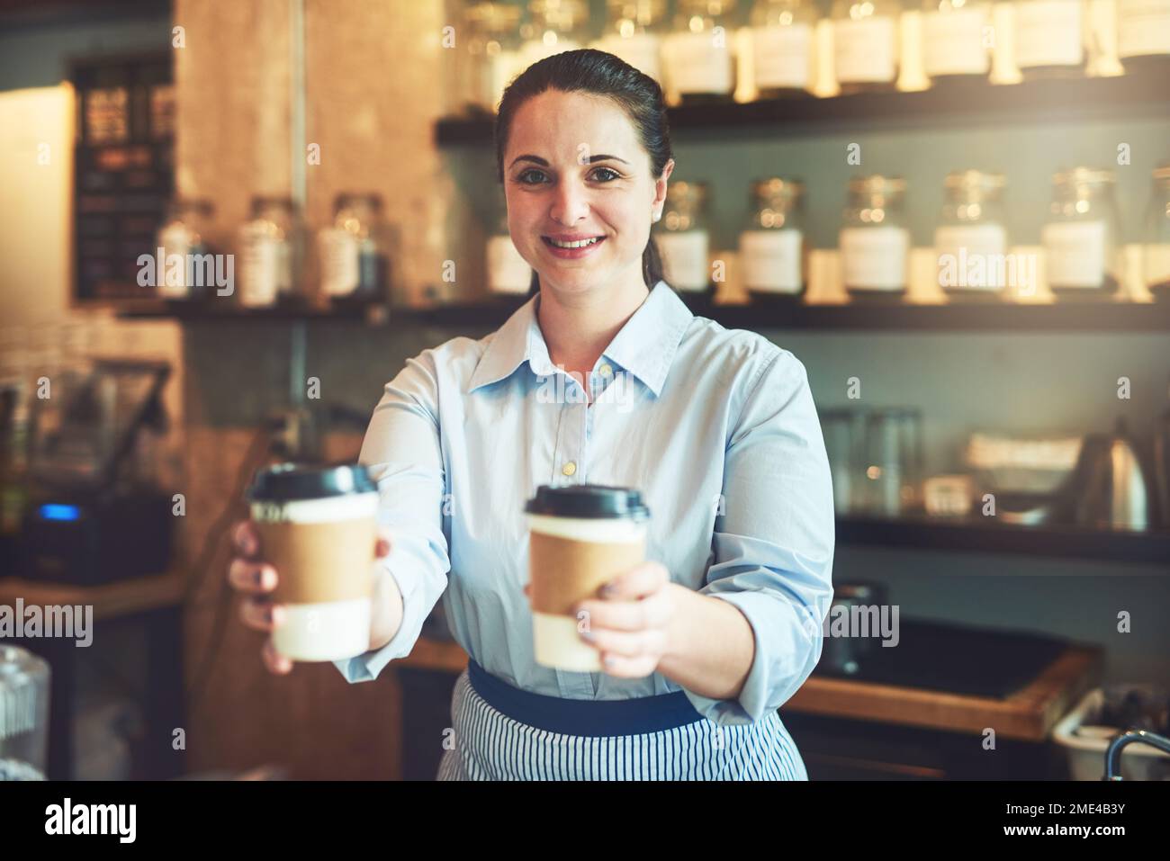 Venez vous procurer votre tasse de confort ici. Portrait d'un jeune barista qui tient des tasses de café dans un café. Banque D'Images