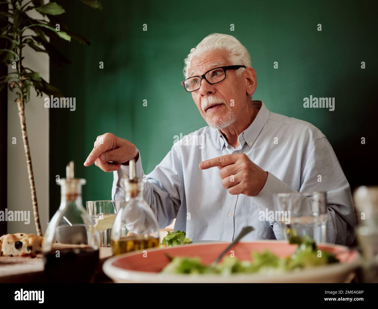 Homme aux cheveux blancs assis à la table du déjeuner en faisant des gestes Banque D'Images