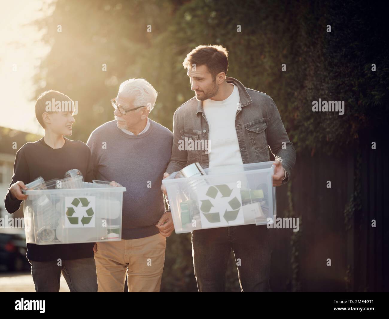 Grandfarher, père et fils debout à l'extérieur transportant des boîtes de recyclage avec des déchets séparés Banque D'Images