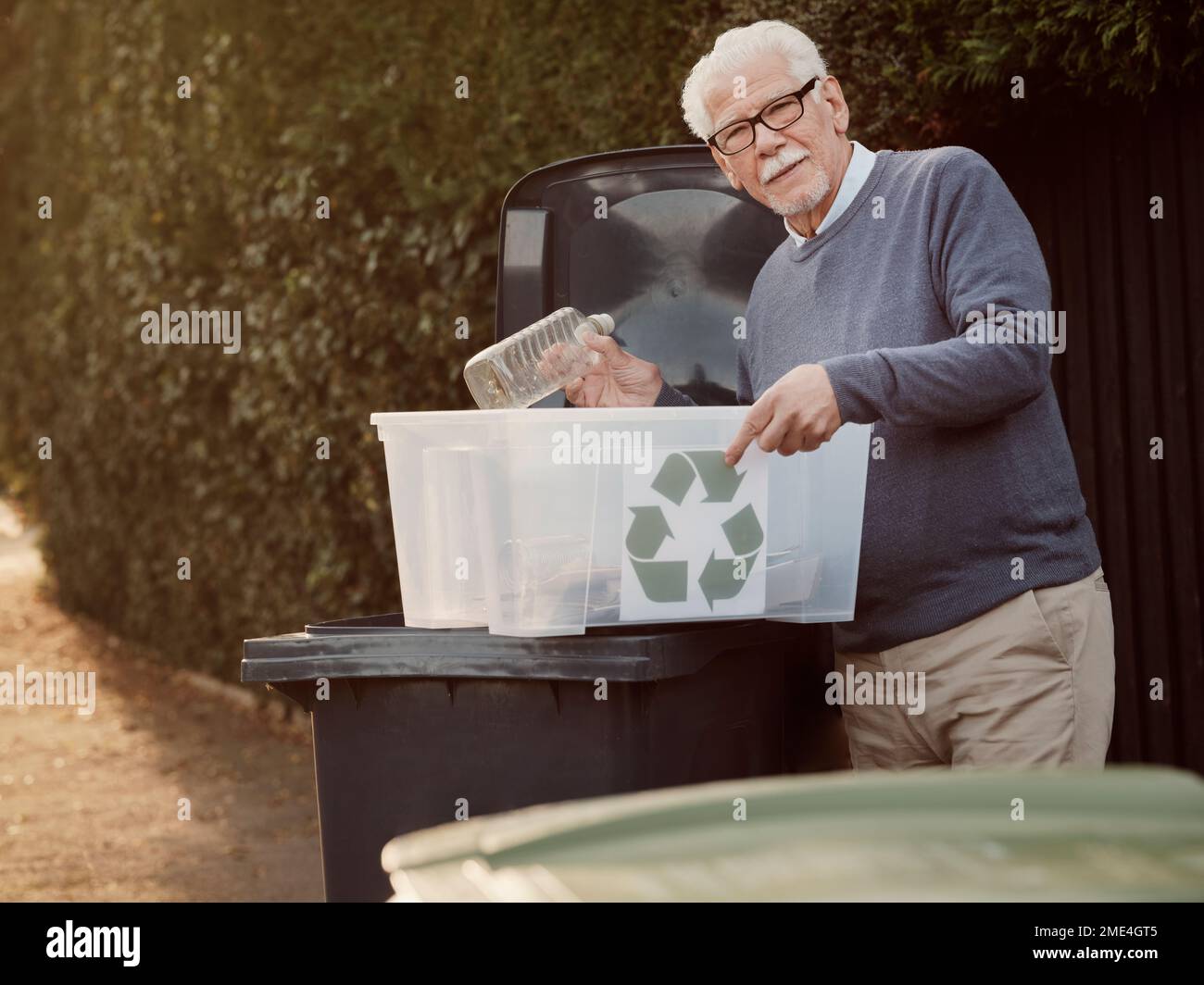 Homme senior plaçant les déchets de recyclage séparés dans la poubelle Banque D'Images