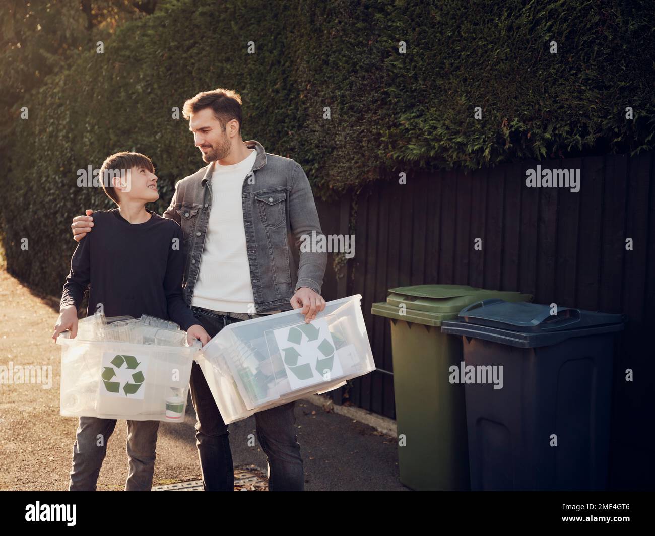 Père et fils debout à l'extérieur transportant des boîtes de recyclage avec des déchets séparés Banque D'Images