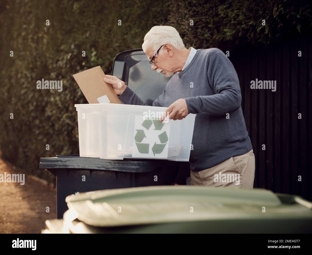 Homme senior plaçant les déchets de recyclage séparés dans la poubelle Banque D'Images