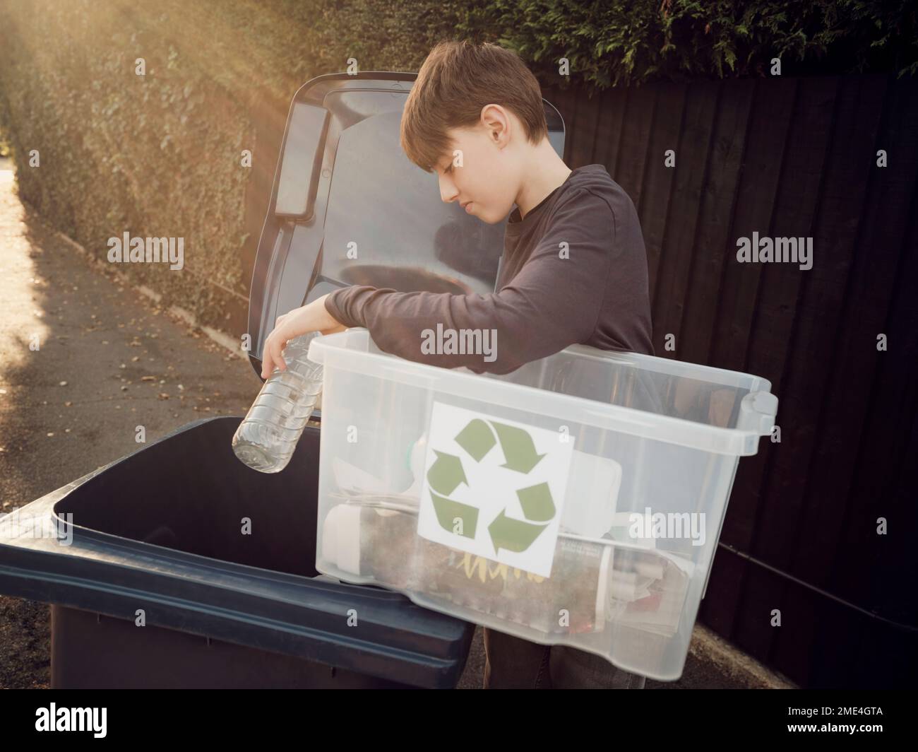 Garçon mettant les déchets de recyclage séparés dans la poubelle Banque D'Images
