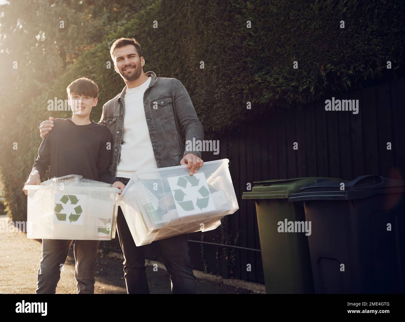 Père et fils debout à l'extérieur transportant des boîtes de recyclage avec des déchets séparés Banque D'Images