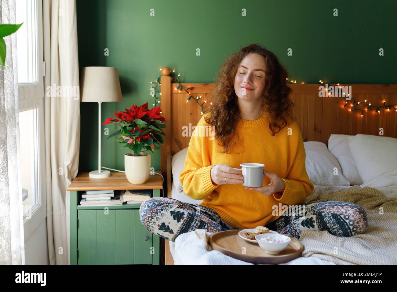 Femme avec les yeux fermés tenant une tasse de thé dans le lit à la maison Banque D'Images