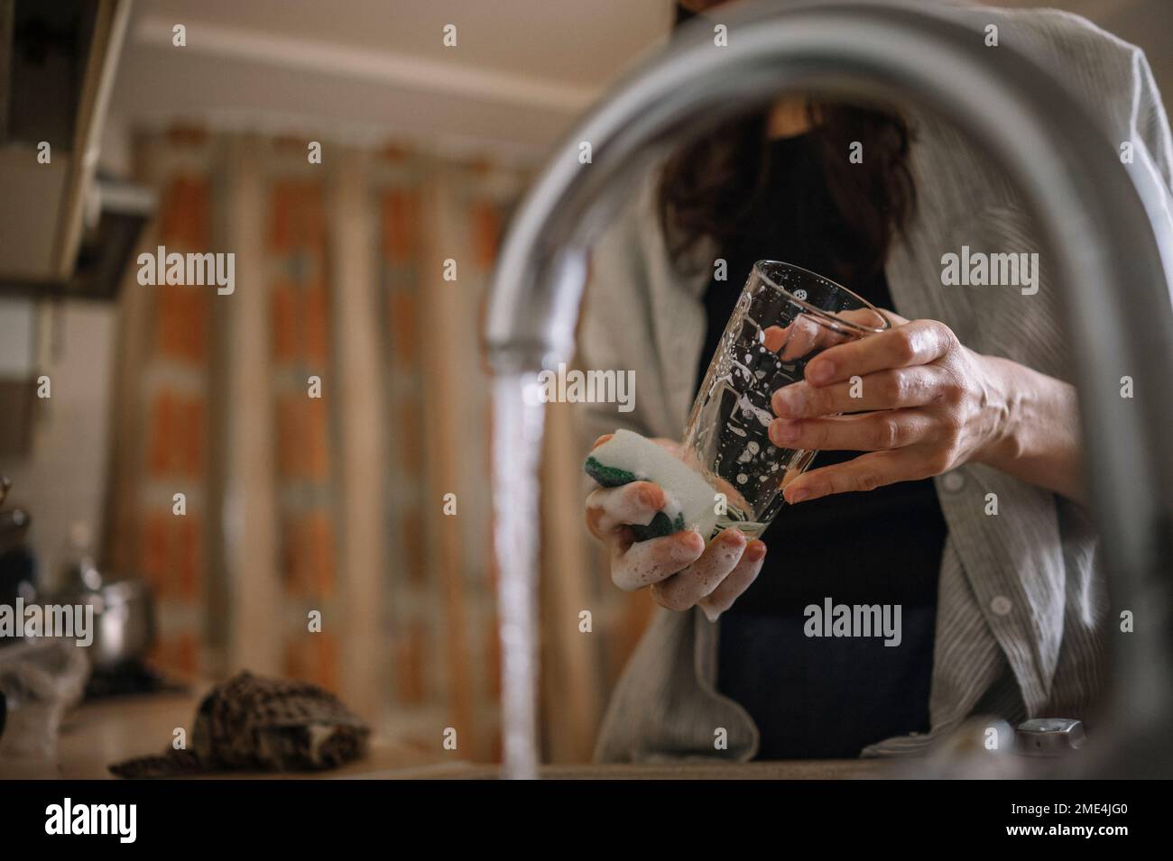 Femme lavant du verre à boire devant l'eau courante du robinet à la maison Banque D'Images