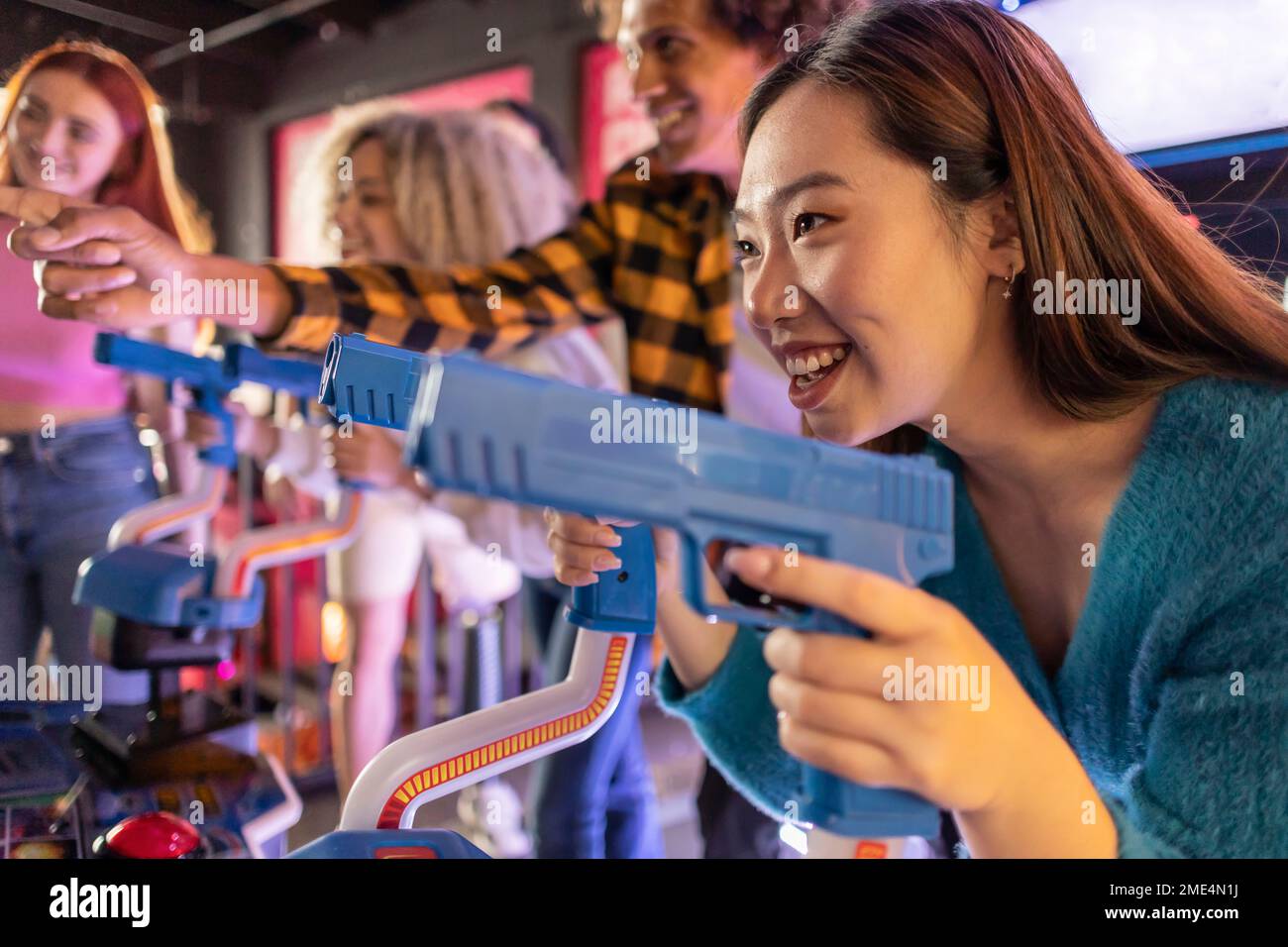 Bonne jeune femme qui apprécie le jeu de tir avec des amis à l'arcade Banque D'Images