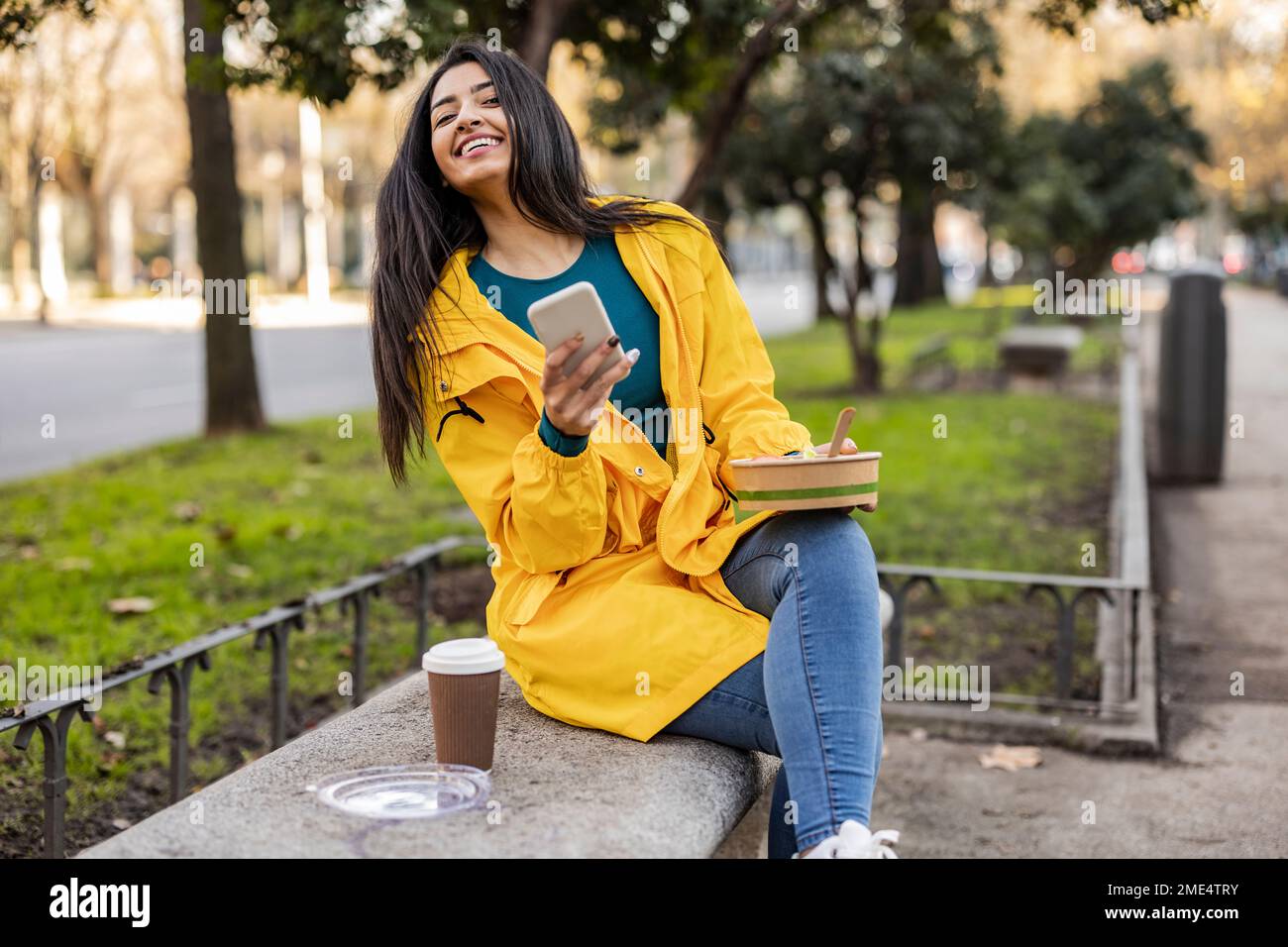 Jeune femme heureuse avec bol et smartphone assis sur le siège Banque D'Images