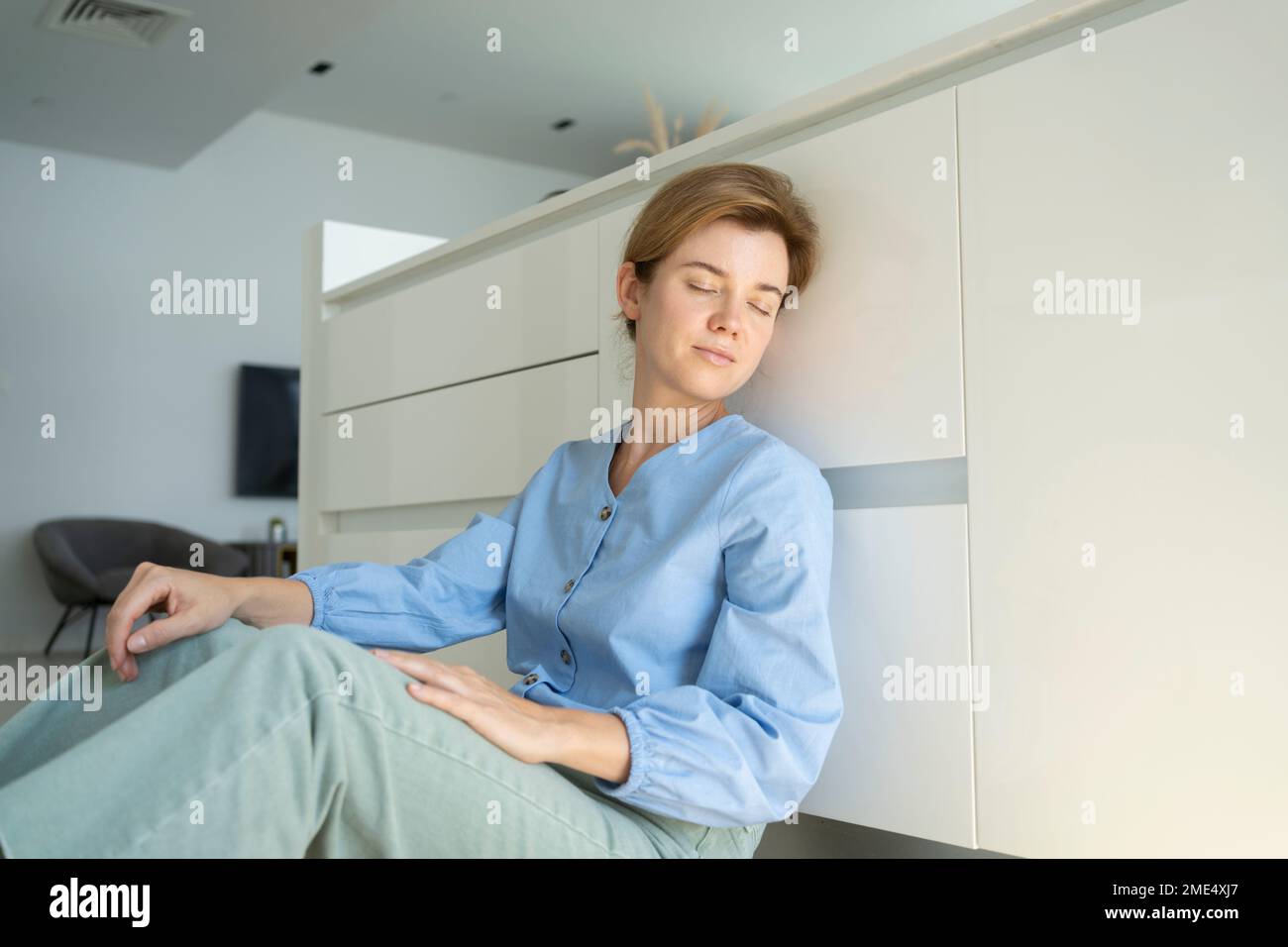 Femme avec les yeux fermés assis près des armoires dans la cuisine à la maison Banque D'Images