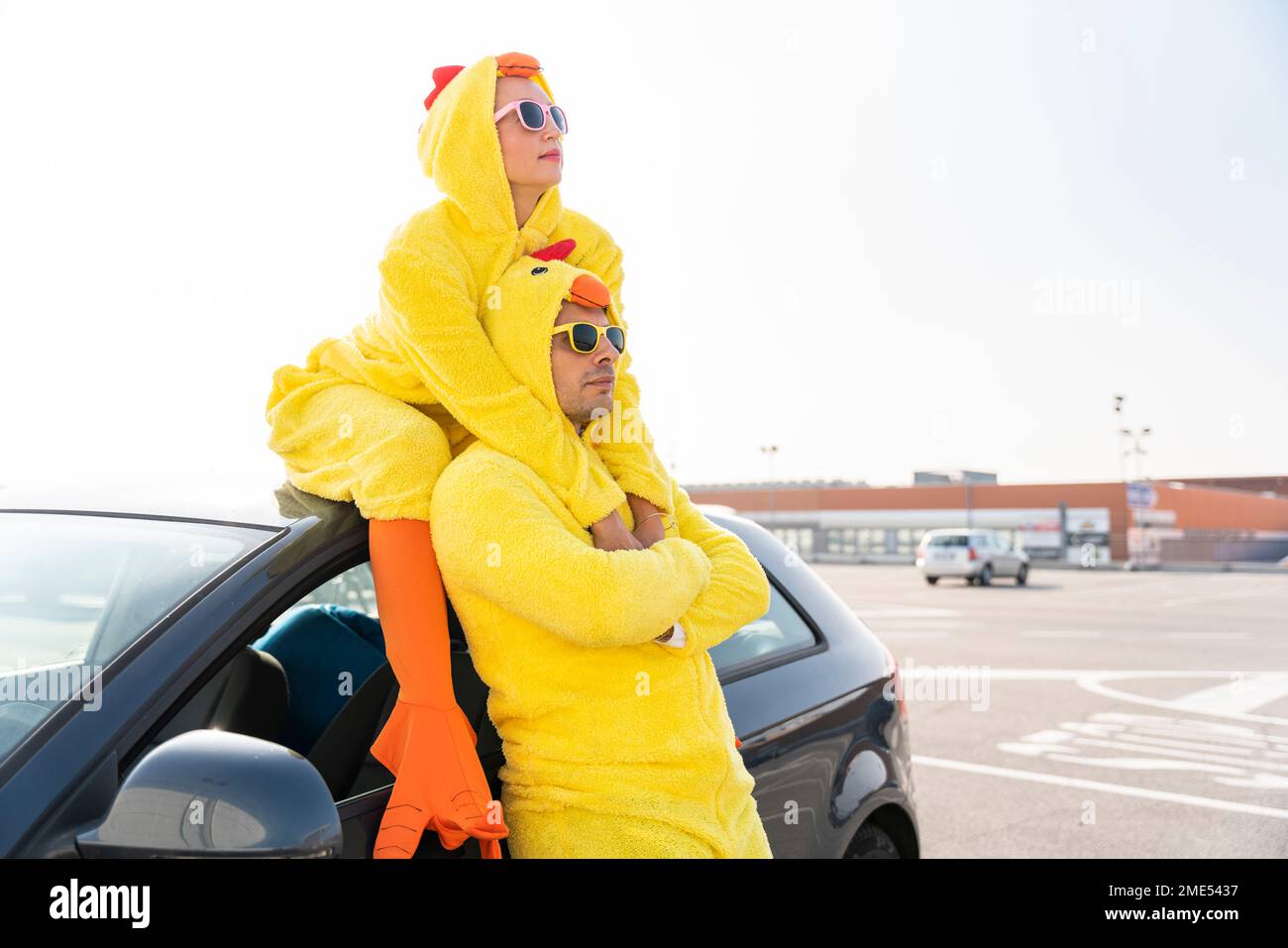 Amis en costume de poulet avec voiture au parking Banque D'Images