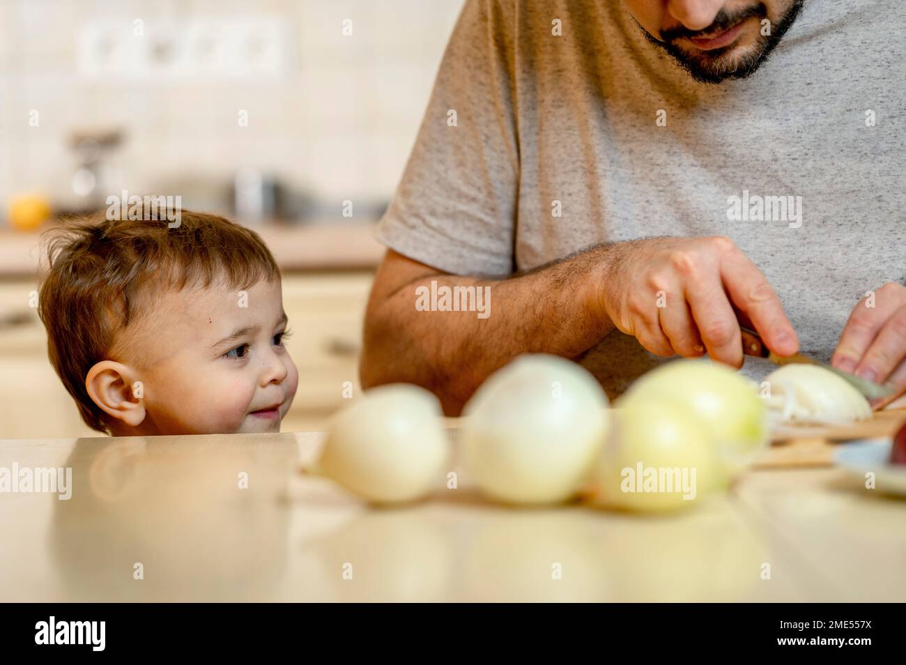 Garçon regardant le père coupant l'oignon dans la cuisine à la maison Banque D'Images