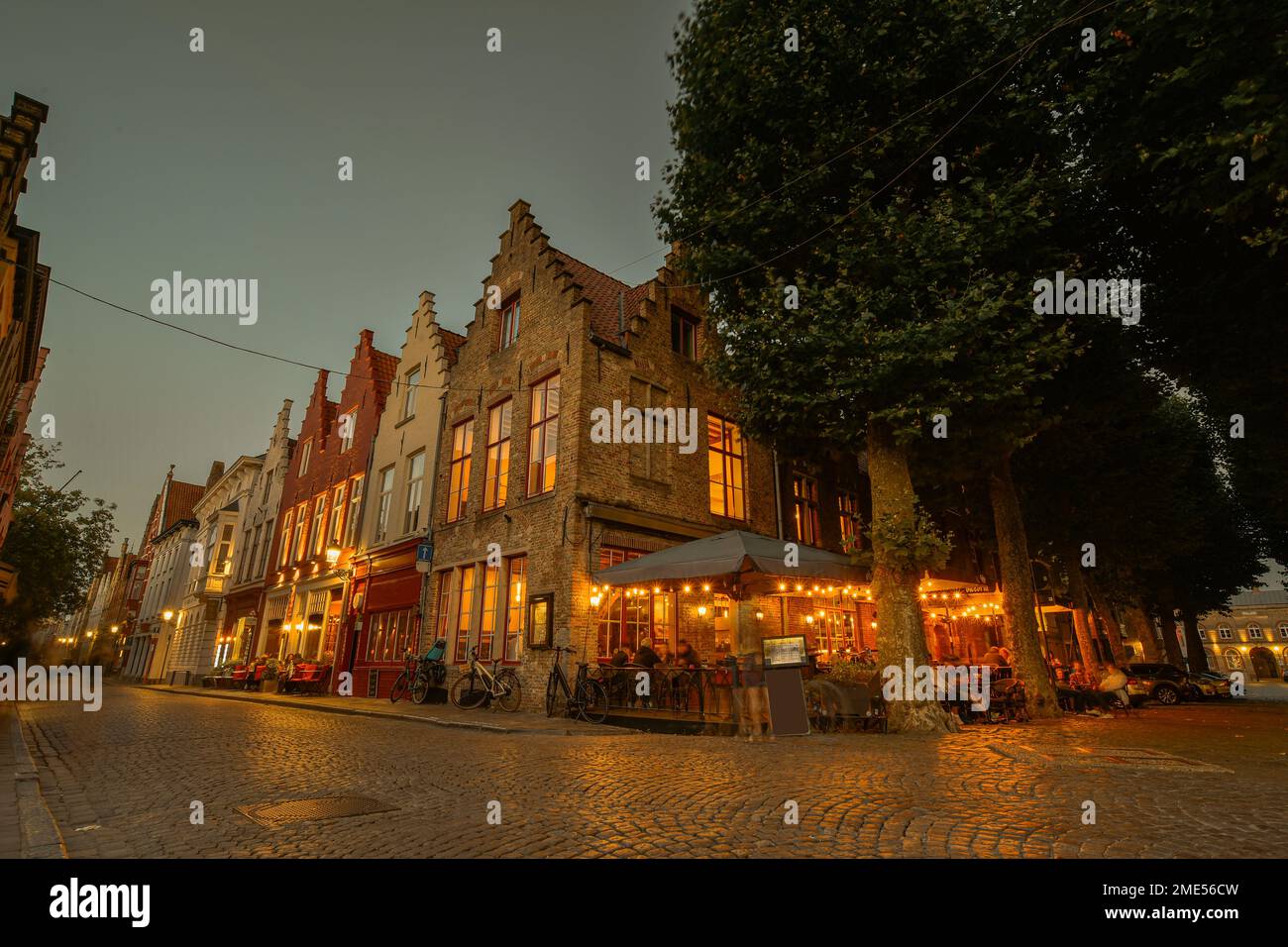 Belgique, Flandre Occidentale, Bruges, rue Cobblestone s'étendant devant un café-terrasse et une rangée de maisons de ville au crépuscule Banque D'Images