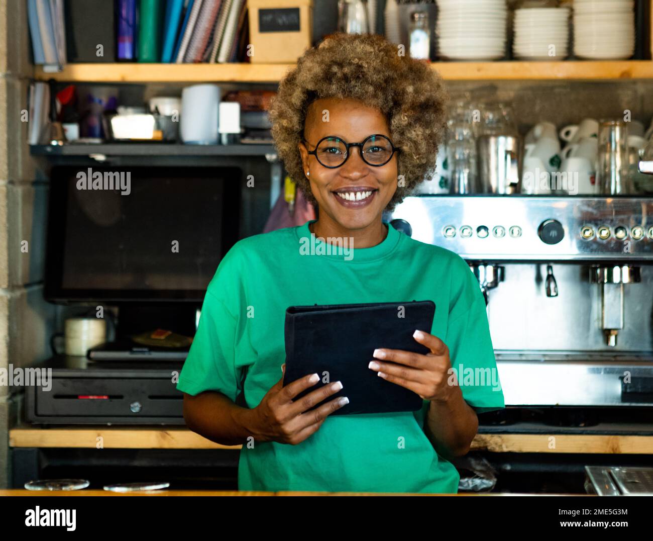 Portrait d'une jeune femme afro-américaine avec une tablette regardant l'appareil photo dans un pub. Femme entrepreneuriale, petite entreprise Banque D'Images