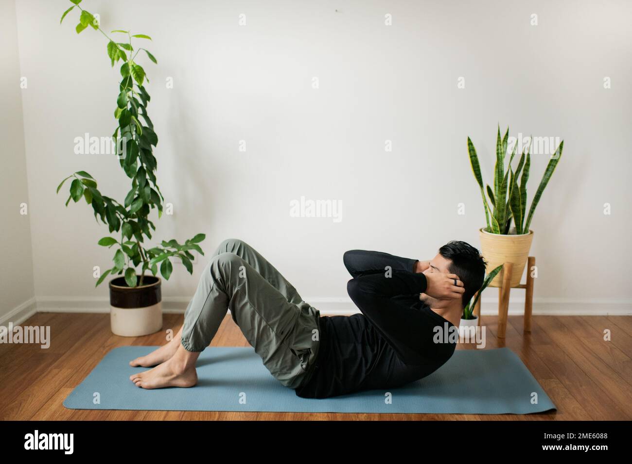 Jeune homme s'exerçant à la maison sur le tapis de yoga près des plantes Banque D'Images