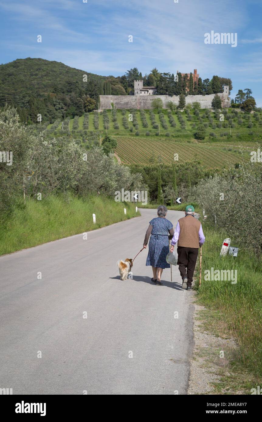 Couple plus âgé marchant avec un chien en laisse le long de la route de campagne en Toscane, Italie. Banque D'Images