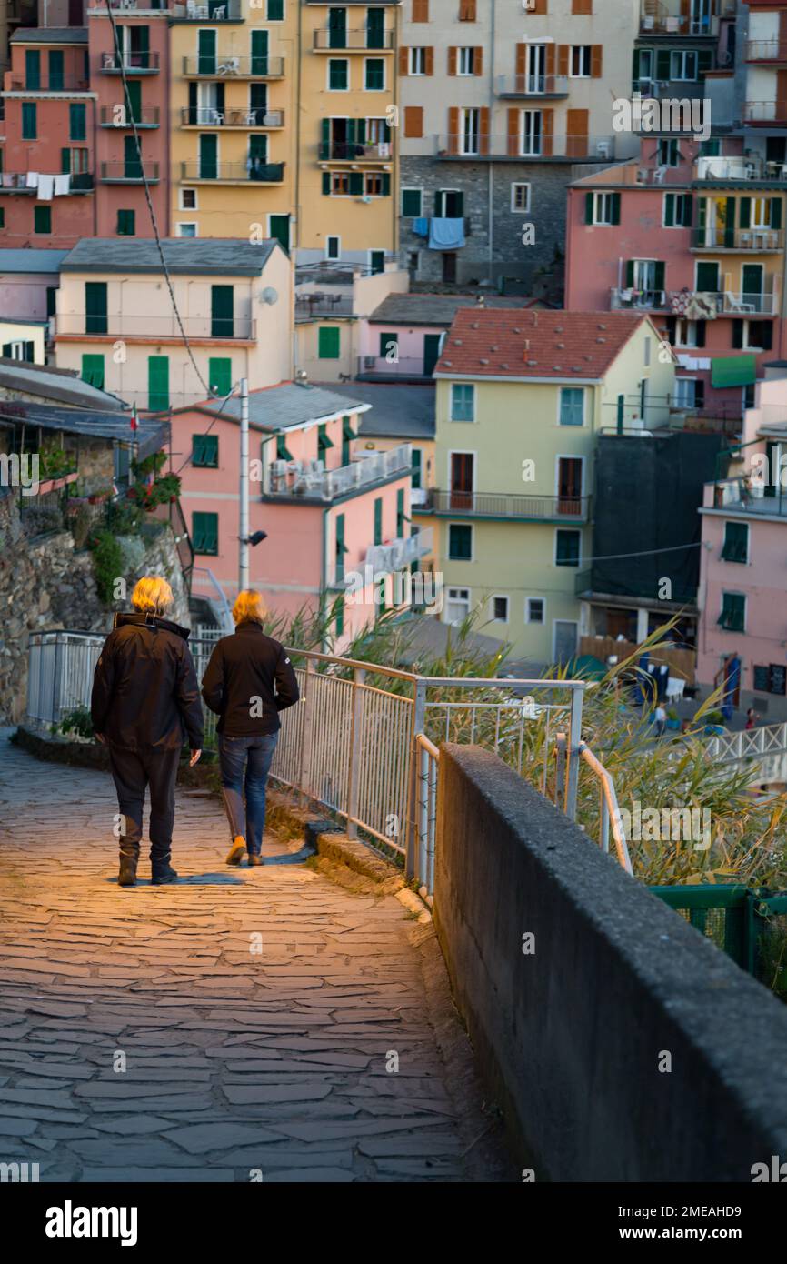 Deux femmes marchant vers le bas de la passerelle éclairée en début de soirée à Manarola, Cinque Terre, Italie. Banque D'Images