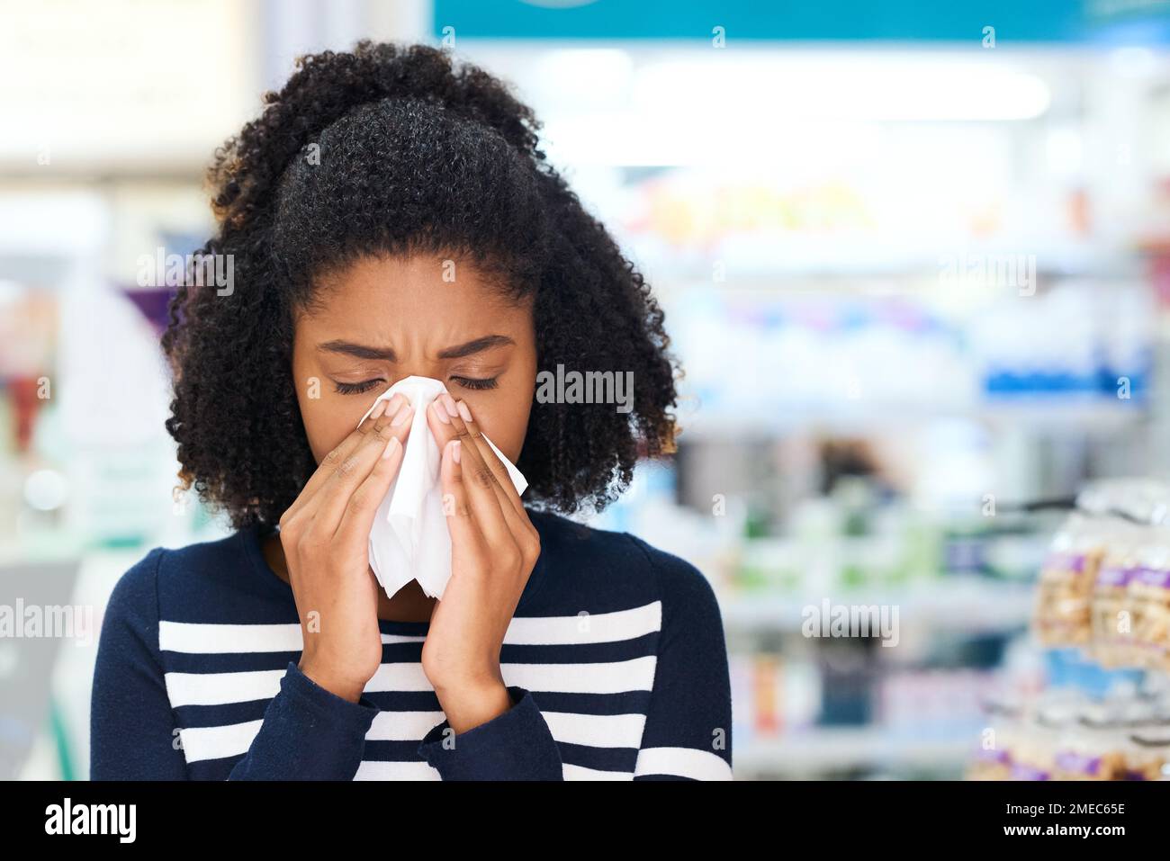 Traitez vos symptômes avant qu'ils ne s'aggravent. une jeune femme soufflant le nez dans une pharmacie. Banque D'Images