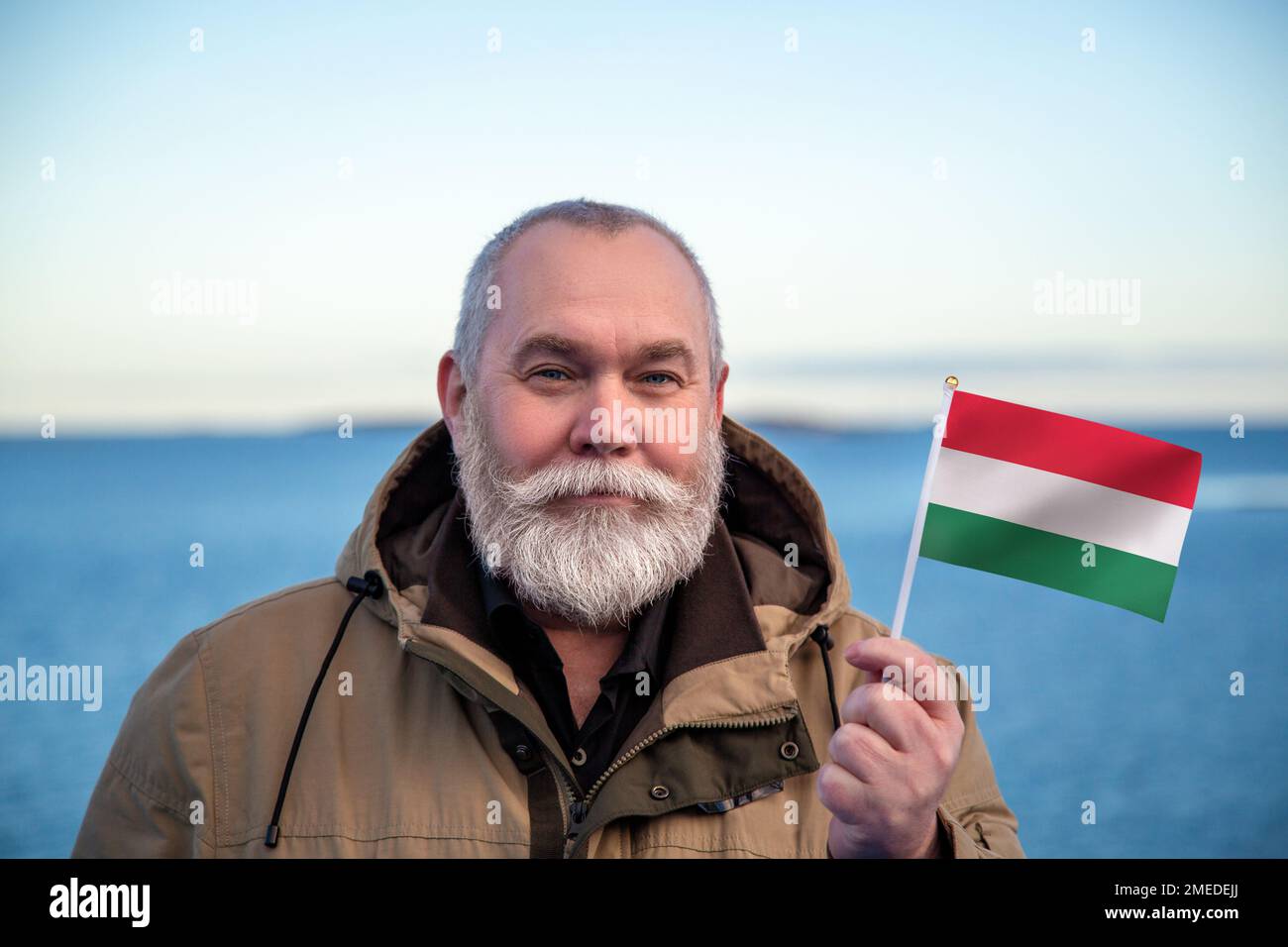 Homme portant le drapeau de la Hongrie. Portrait d'un homme âgé avec un drapeau national hongrois. Visitez le concept de Hongrie. Homme plus âgé de 55 60 ans voyageant en hiver Banque D'Images