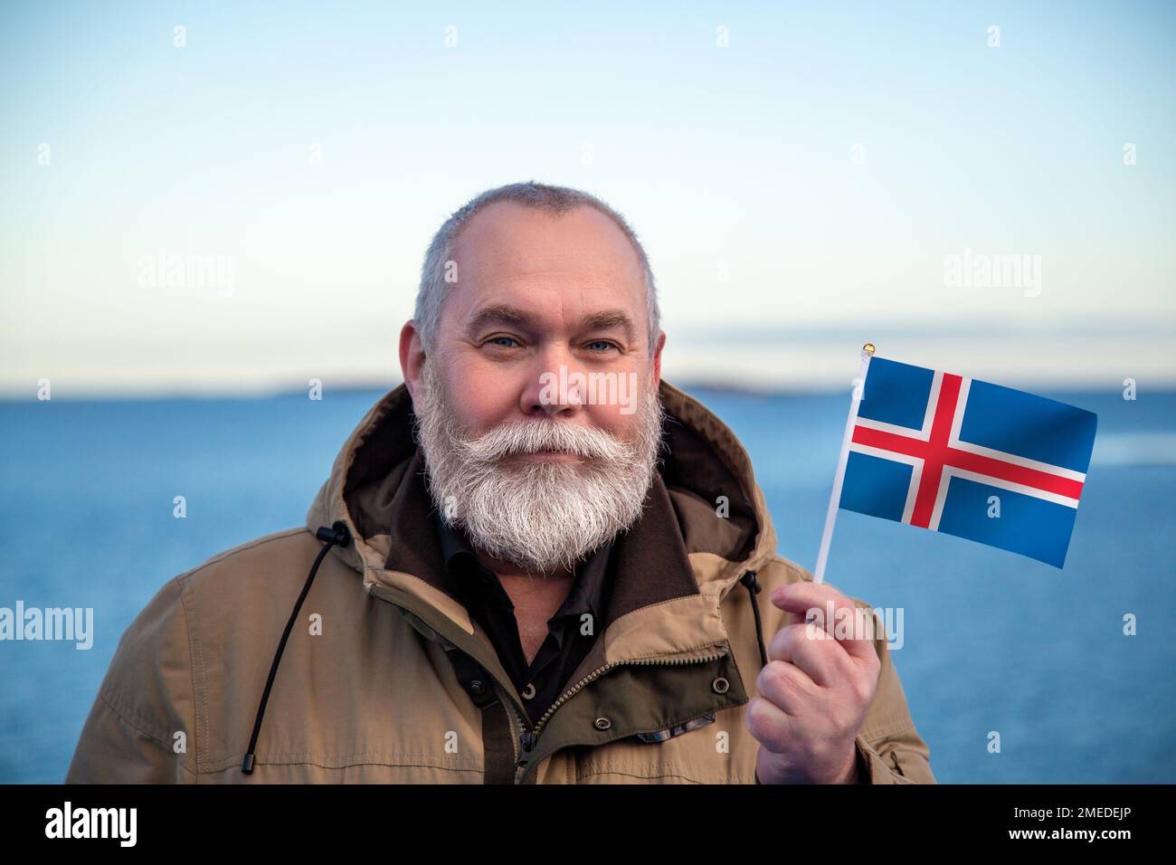Homme portant le drapeau islandais. Portrait d'un homme plus âgé avec un drapeau islandais national. Visiter Iceland concept. Homme plus âgé de 55 60 ans voyageant en hiver Banque D'Images