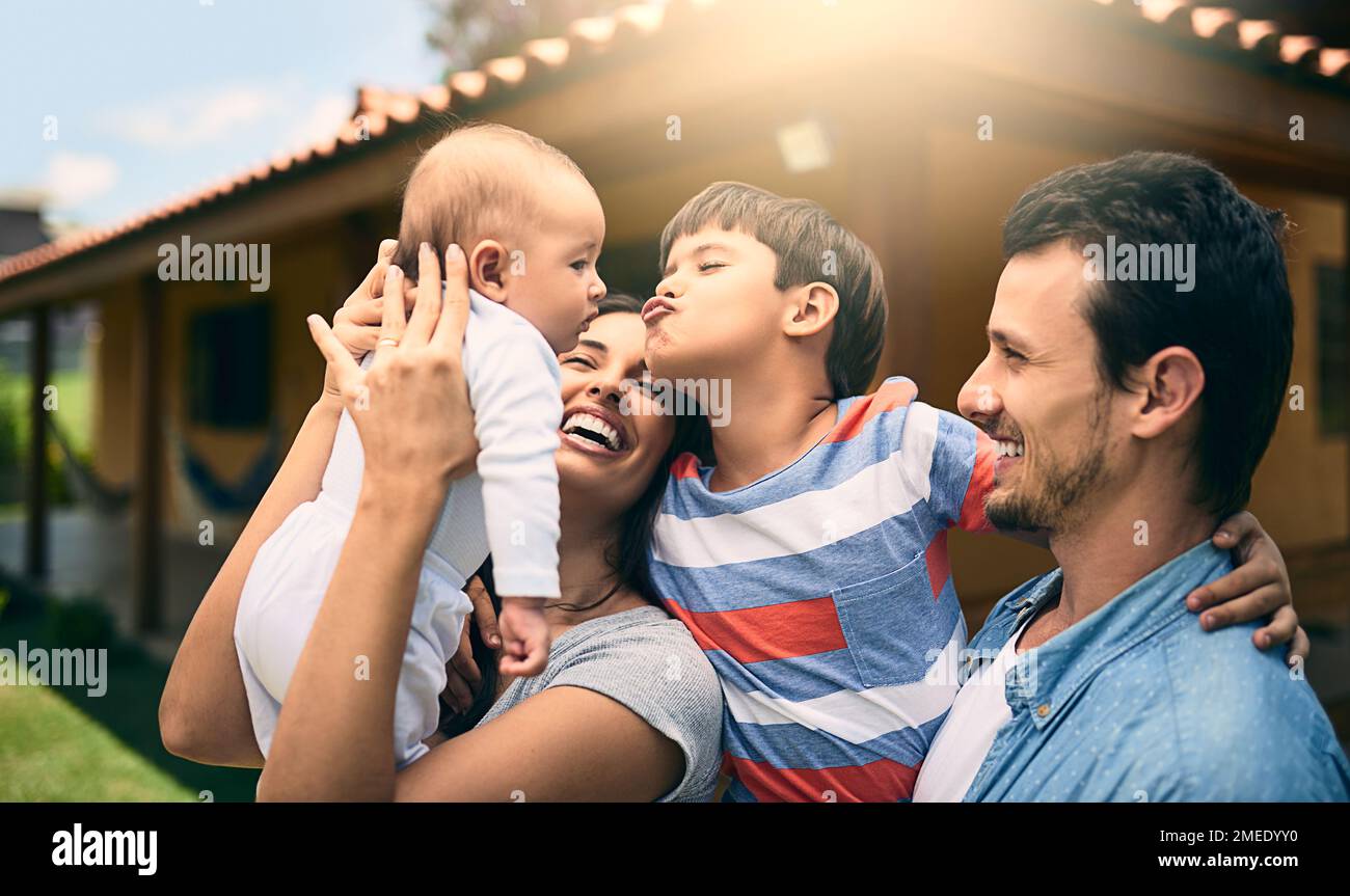 Il voulait toujours un petit frère. une jeune famille heureuse de quatre à l'extérieur avec leur maison en arrière-plan. Banque D'Images